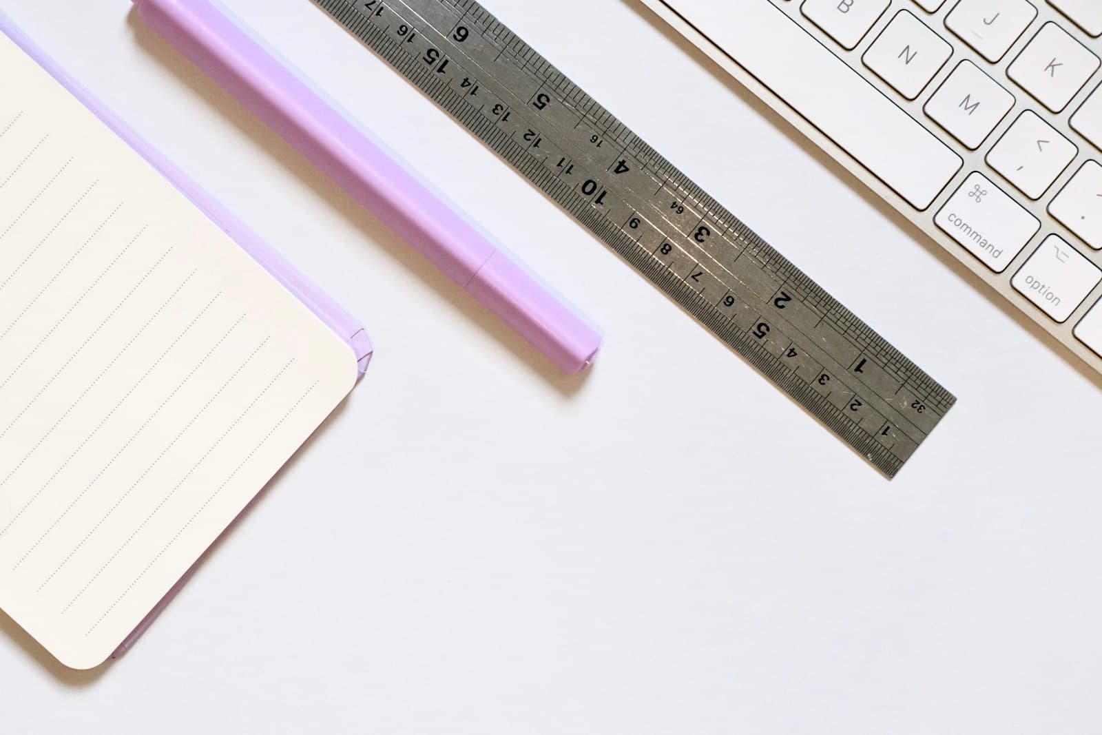 An open notebook, purple pen, ruler, and keyboard on a white desk